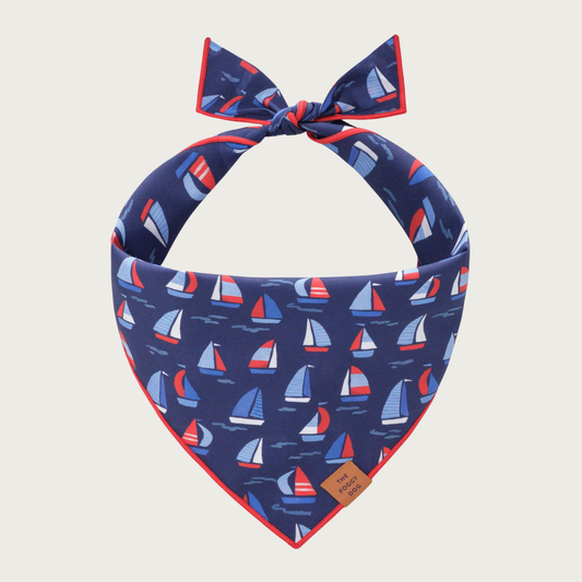 Navy blue dog bandana with sailboat pattern in shades of red, white, and blue.