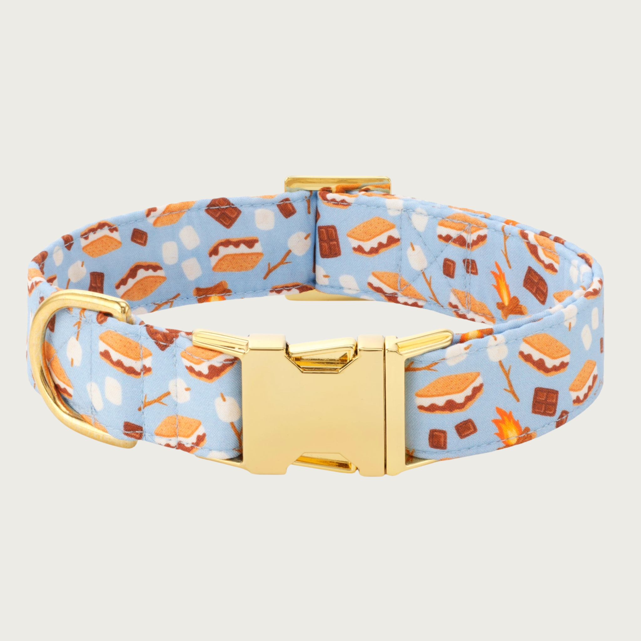 Dog collar with s'mores pattern on a light blue background. The pattern includes illustrated campfires, loose marshmallows, marshmallows on a stick, chocolate bars, and fully assembled s'mores. Features gold-toned hardware.