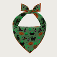 Load image into Gallery viewer, Night view of the bandana when it's glowing in the dark. The glass crystal balls, moons, stars, and bubbling potion in cauldrons all turn a bright green color.
