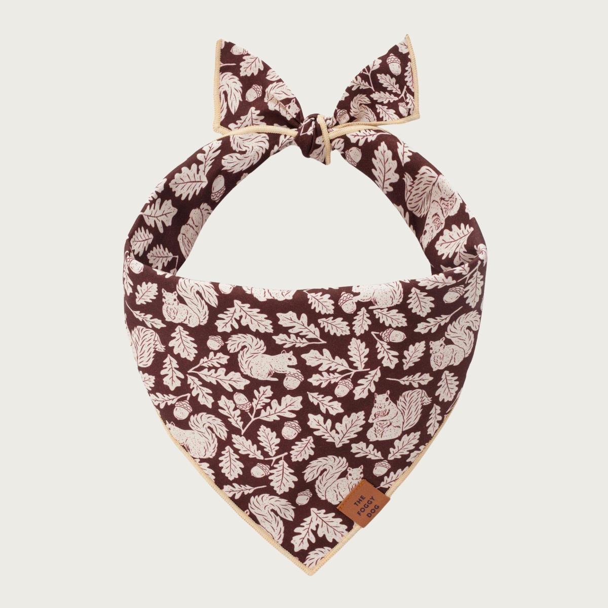 Tied dog bandana featuring a deep brown background with realistic looking, cream colored squirrels, oak leaves, and acorns.