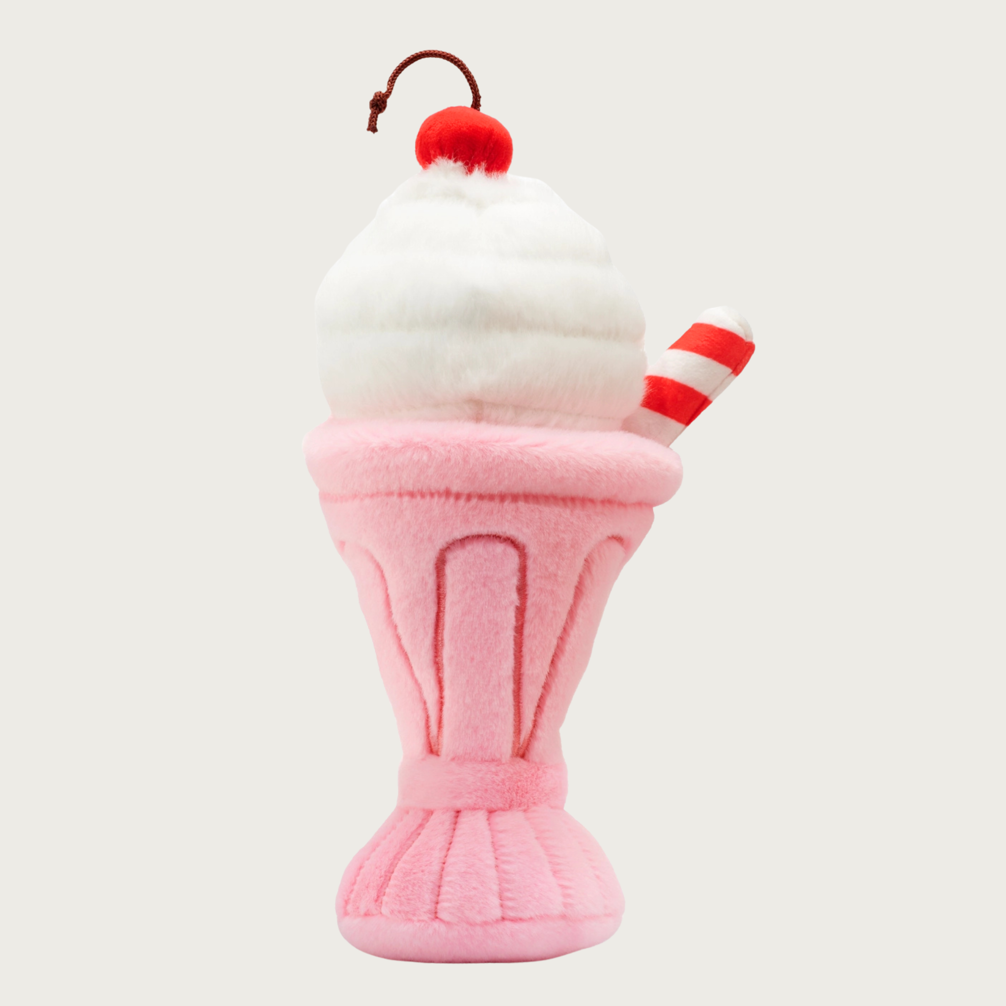 Plush dog toy that looks like an old-time strawberry milkshake. The pink base is shaped like a tapered glass, and there is a white scoop of "ice cream" on top, with a red cherry on top of it. There is also a red & white striped "straw" sticking out of the top of the "glass."