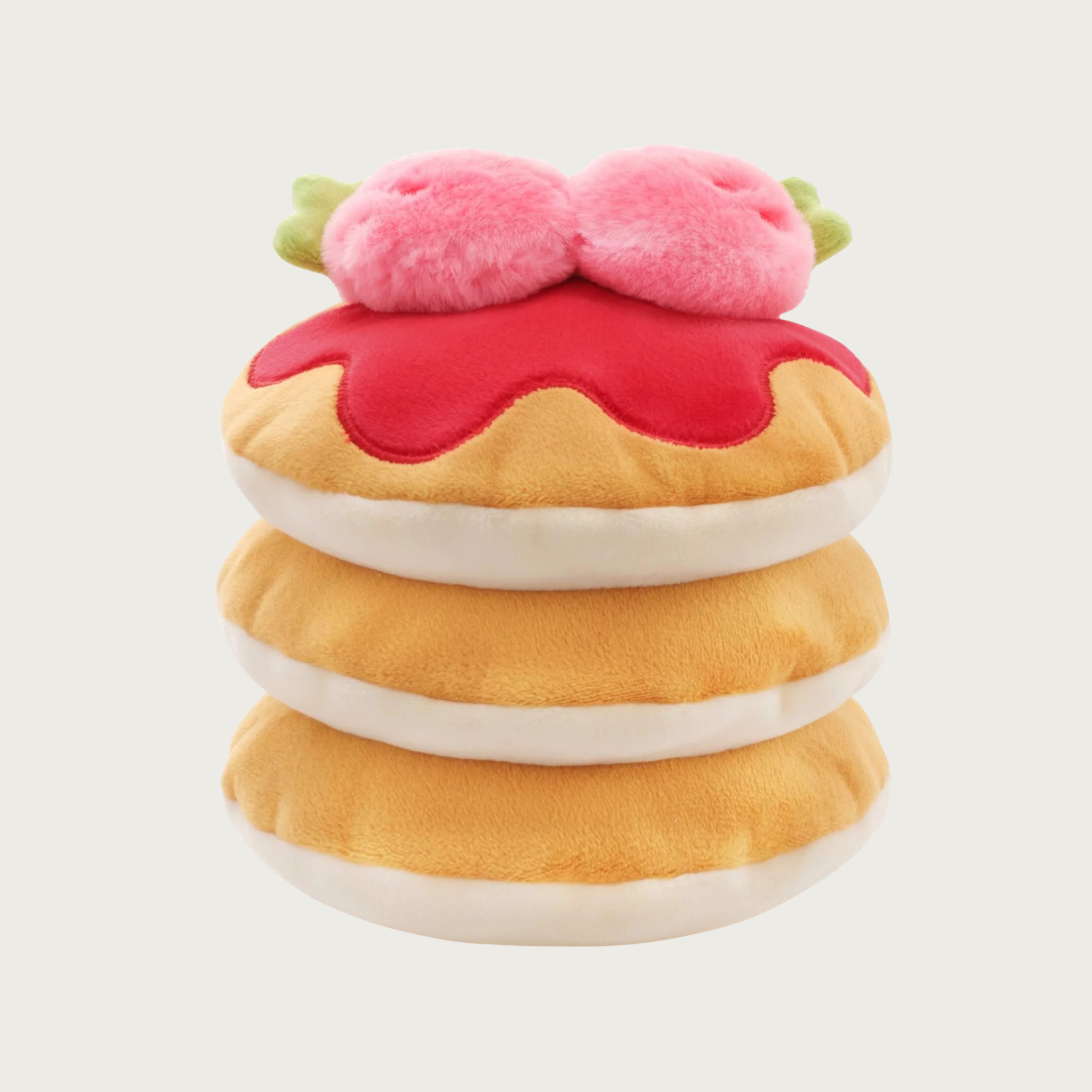 Plush dog toy resembling a stack of layered pancakes. The 3 pancakes are tan on top and cream colored underneath, on the very top one there is a red "puddle" of syrup and two large plush strawberries.
