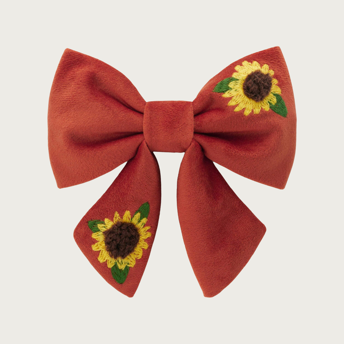 Rust brown lady bow tie for dogs, with two embroidered yellow sunflowers with brown centers and green leaves, in the top right and bottom left of the bow. Looks like a hair bow for a person, with the center bow tie and ends hanging down.