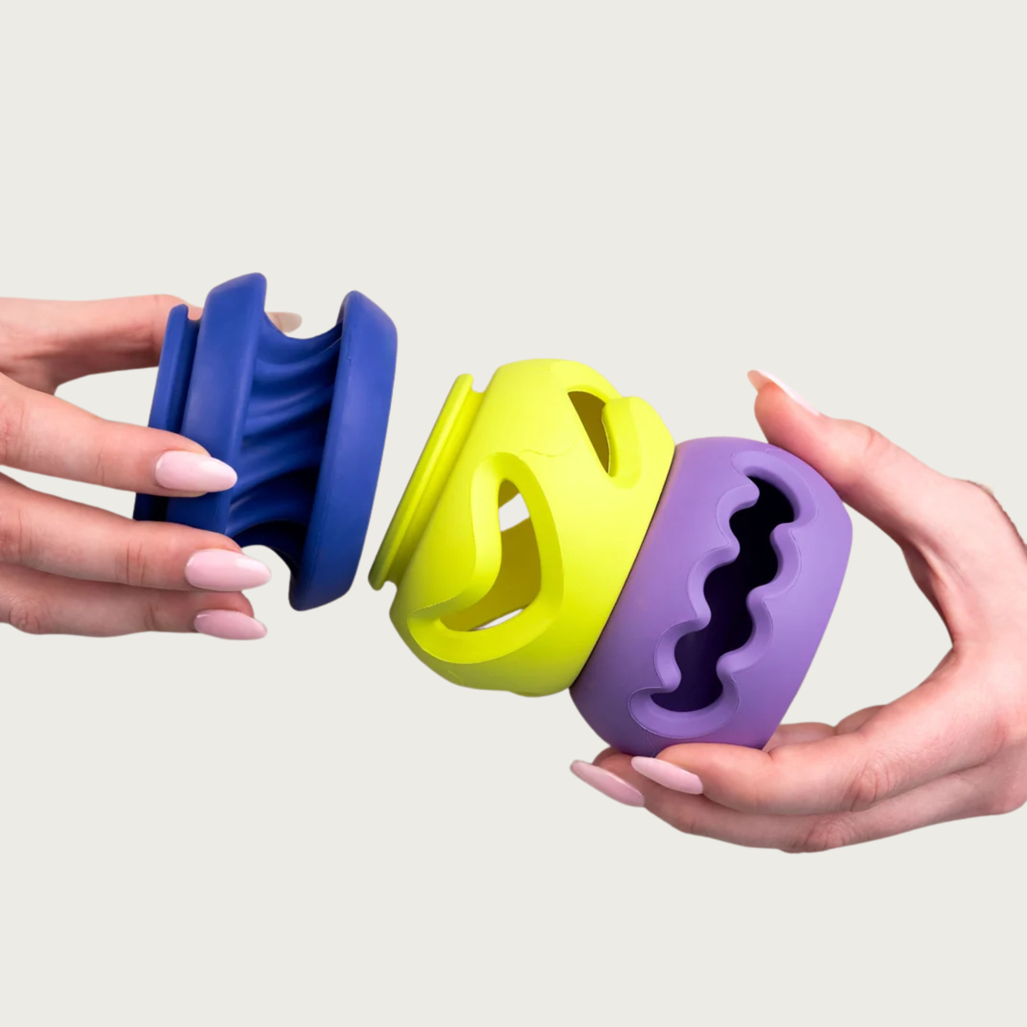 Three rubber PlayStack dog toys in blue, yellow, and purple held by hands, showing how the toys connect.