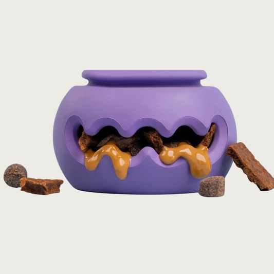 A purple rubber dog toy with wide, wavy cut-out in the center, stuffed with treats and peanut butter visible inside and dripping out.