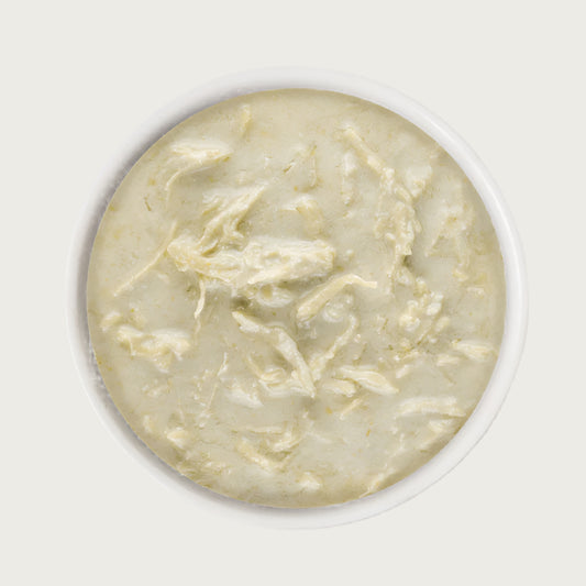 A close-up image of a dish of Weruva Wx Phos Focused Chicken Formula in Gravy. It is beige in color, and shows shreds of chicken in a creamy looking gravy.