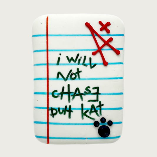 A dog cookie designed to look like a graded school paper with the phrase 'I will not chase duh kat' written in the middle, accented with a black paw print and red A+ mark.