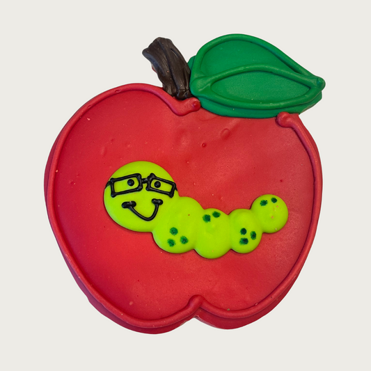 Red apple-shaped dog cookie with a green worm wearing glasses in the middle of it.