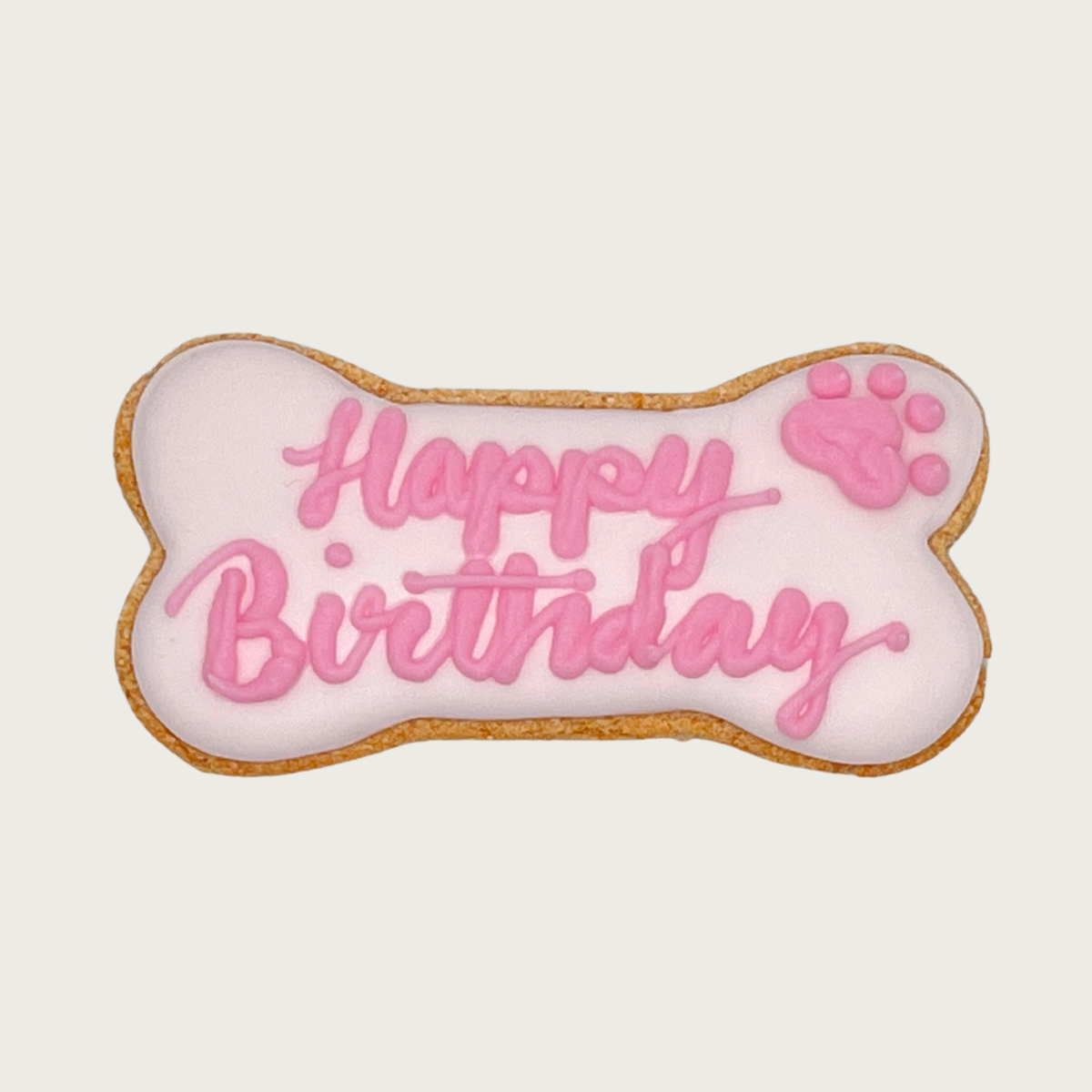 Bone-shaped dog cookie with pale pink icing. "Happy Birthday" is handwritten in script, in bubblegum pink, with a bubblegum pink paw print in the top right corner.