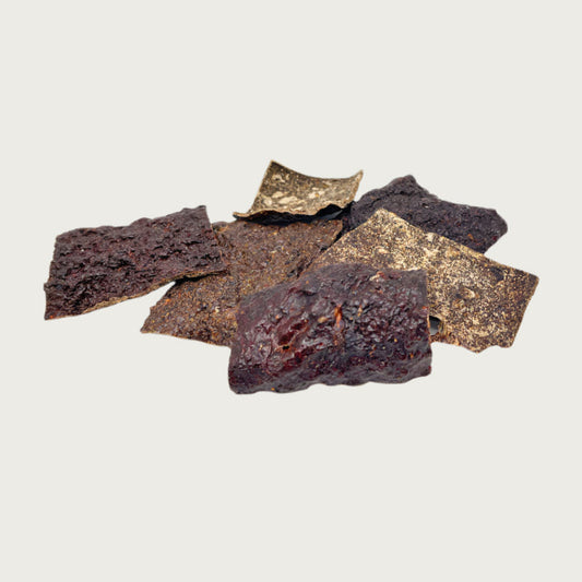 Close-up of a small pile of Wet Nose Beef Crispies treats. They are dark brown, thin squares about 2.5" wide, with a bumpy texture.