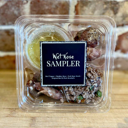 A plastic, sectioned to-go container labeled 'Wet Nose SAMPLER' with an assortment of fresh food for pets, including beef topper, pork bone broth, original meatballs, and cheddar brats.