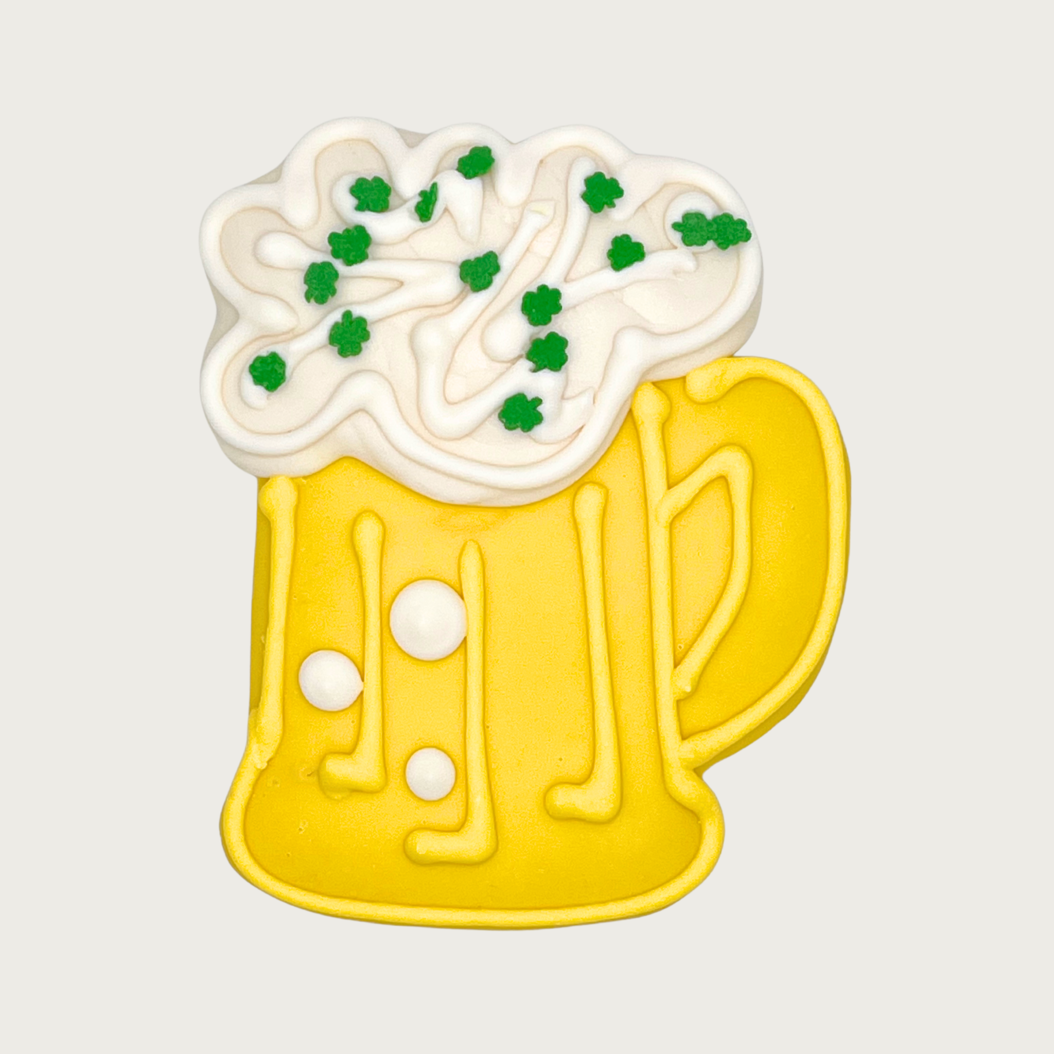 Dog cookie shaped like a yellow beer mug with white foam and green clover shaped sprinkles.