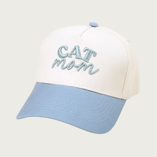 Two-toned baseball cap with ivory body and pale blue bill & button on top. The cap reads "CAT mom" in embroidered pale blue text-"CAT" is in all caps, and "mom" is in lower case script text.