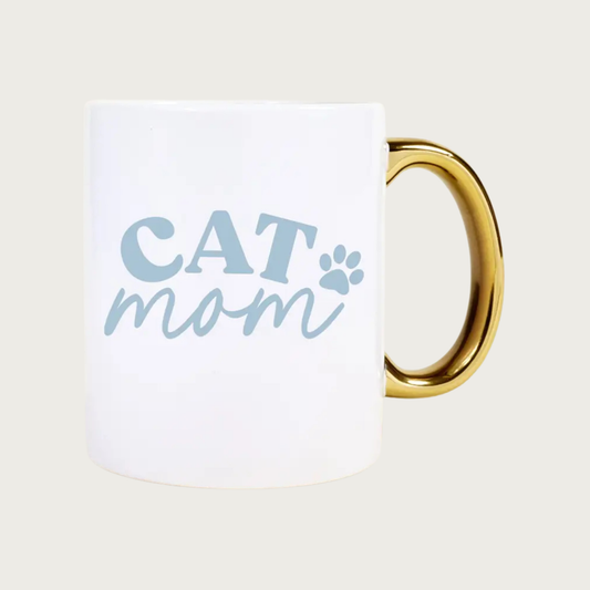 White mug with 'CAT mom' text and paw print in light blue with shiny gold handle. "CAT" is in all caps and "mom" is in lower case script text.
