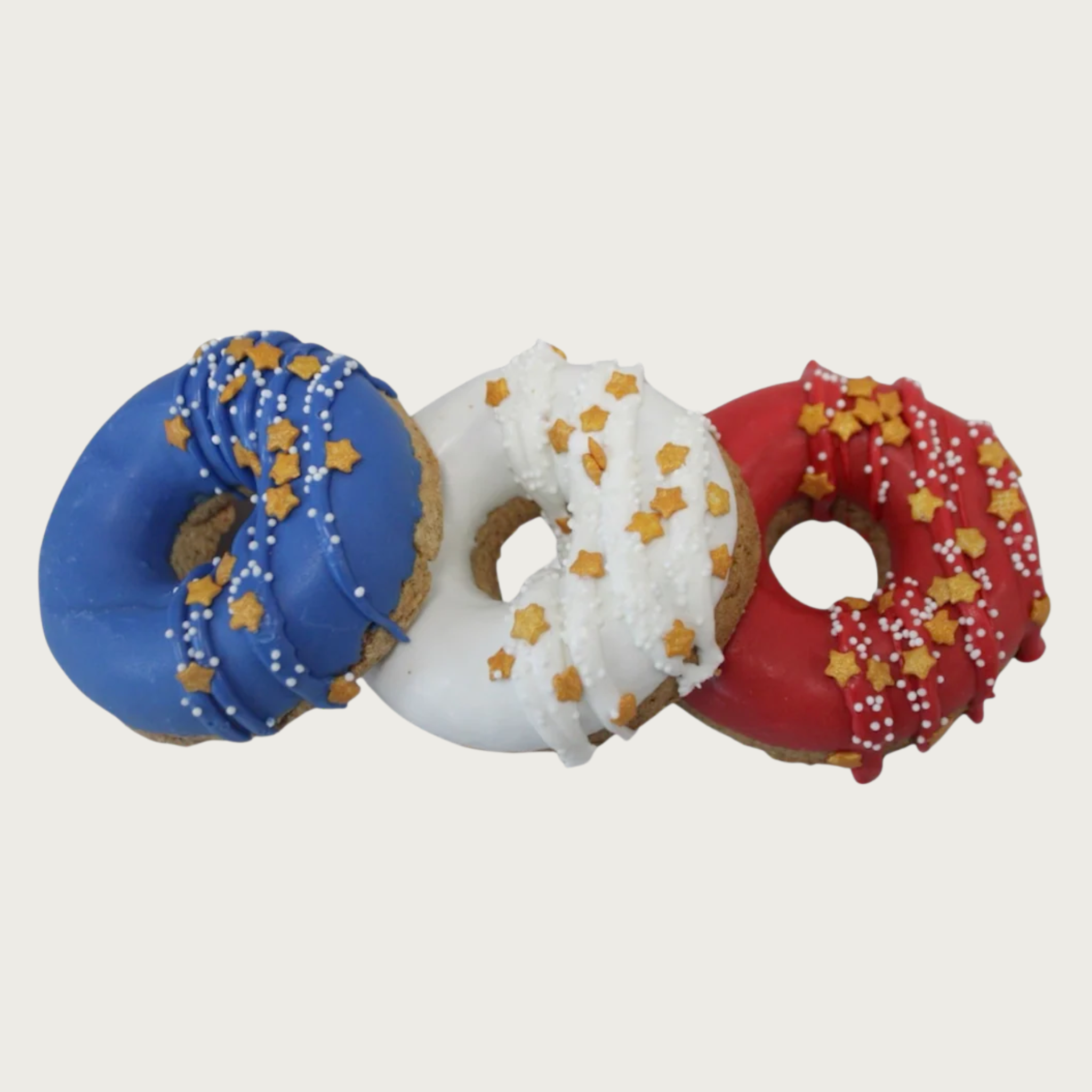 A trio of donut shaped dog cookies, decorated with blue, white, and red icing. Each is one solid color, and has gold star decorettes and white non-pareils.