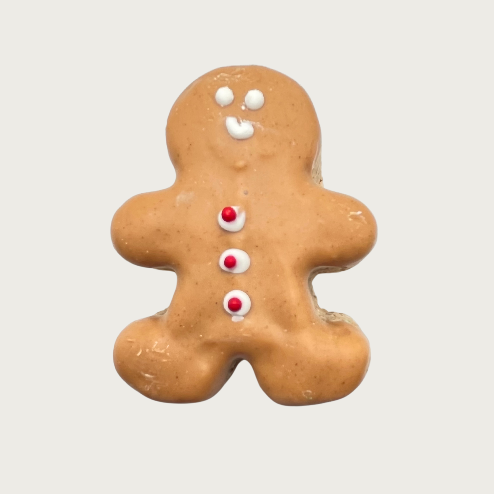 Tan, gingerbread man shaped dog cookie with a simple white smiley face and three red & white buttons down its chest.