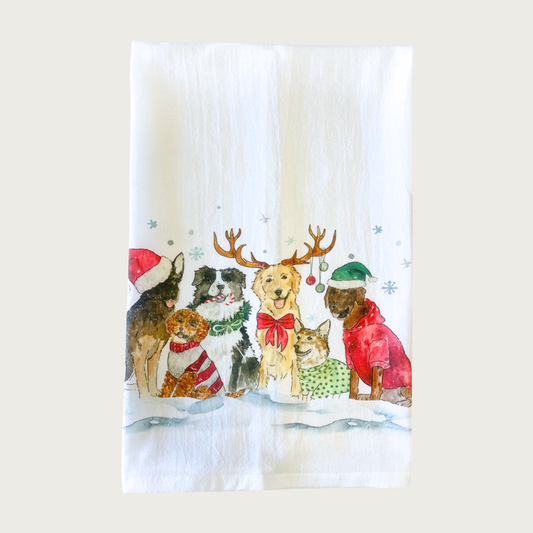 Decorative Christmas-themed tea towel with six different dog breeds on the bottom half of the towel, wearing festive hats, scarves, sweaters and bows. White towel with dog illustration that looks like it was done in ink & watercolor.