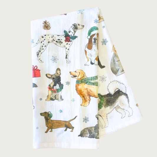 Decorative Christmas-themed tea towel with many different dog breeds, wearing festive hats, scarves, wreaths and bows. White towel with dog illustrations that looks like they were done in ink & watercolor.