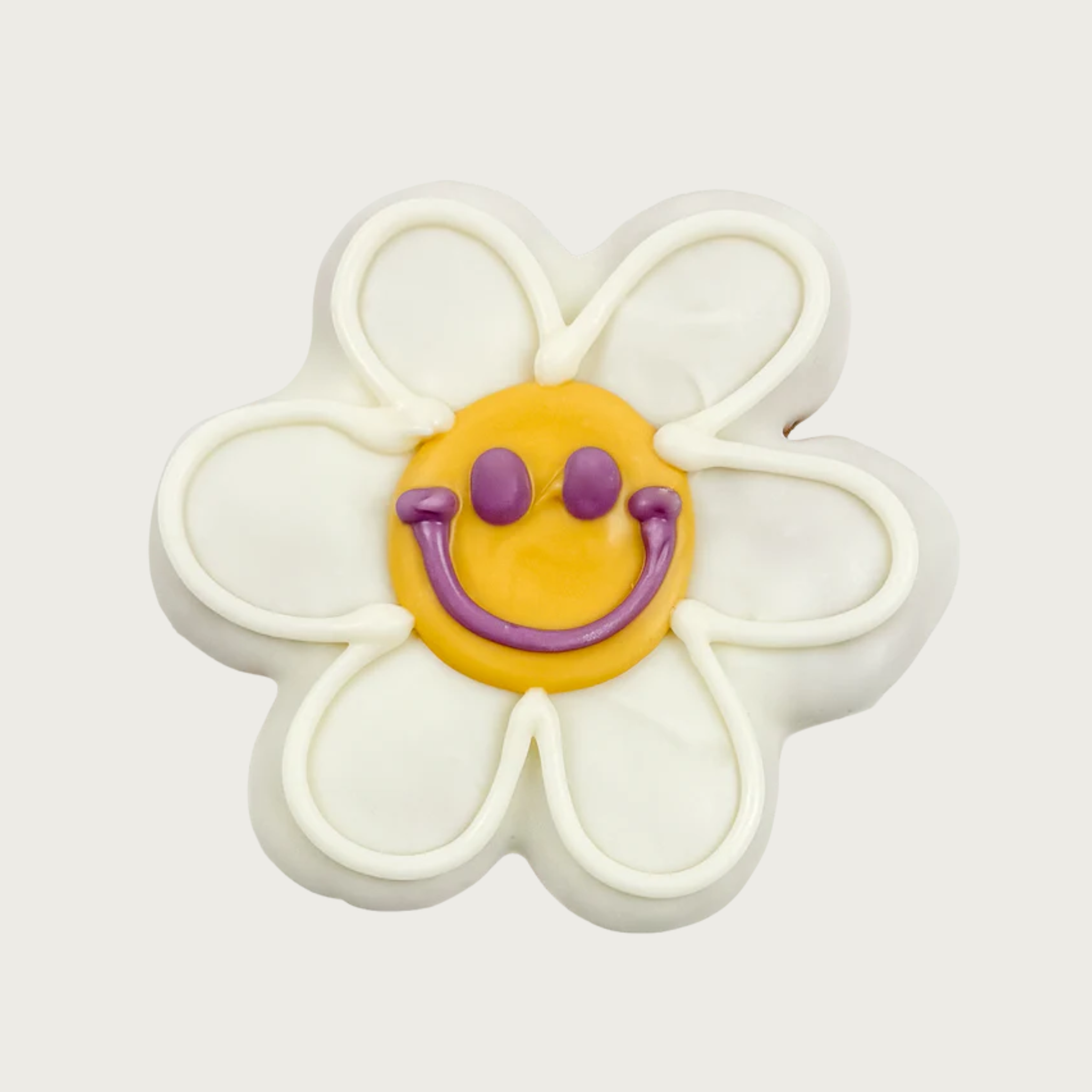 Dog cookie shaped like a white daisy with round yellow center, and a simple smiley face piped in purple icing.