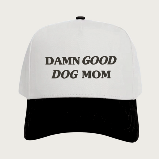 Black and cream baseball cap with 'Damn Good Dog Mom' text in black. Cap body is cream, bill is black.
