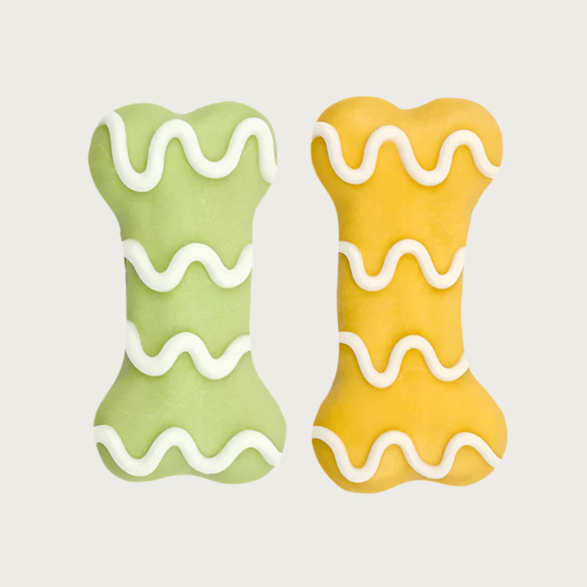 Two dog cookies shaped like dog bones, one is light green and the other is yellow, both have wavy white icing.