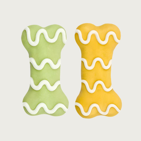 Two dog cookies shaped like dog bones, one is light green and the other is yellow, both have wavy white icing.