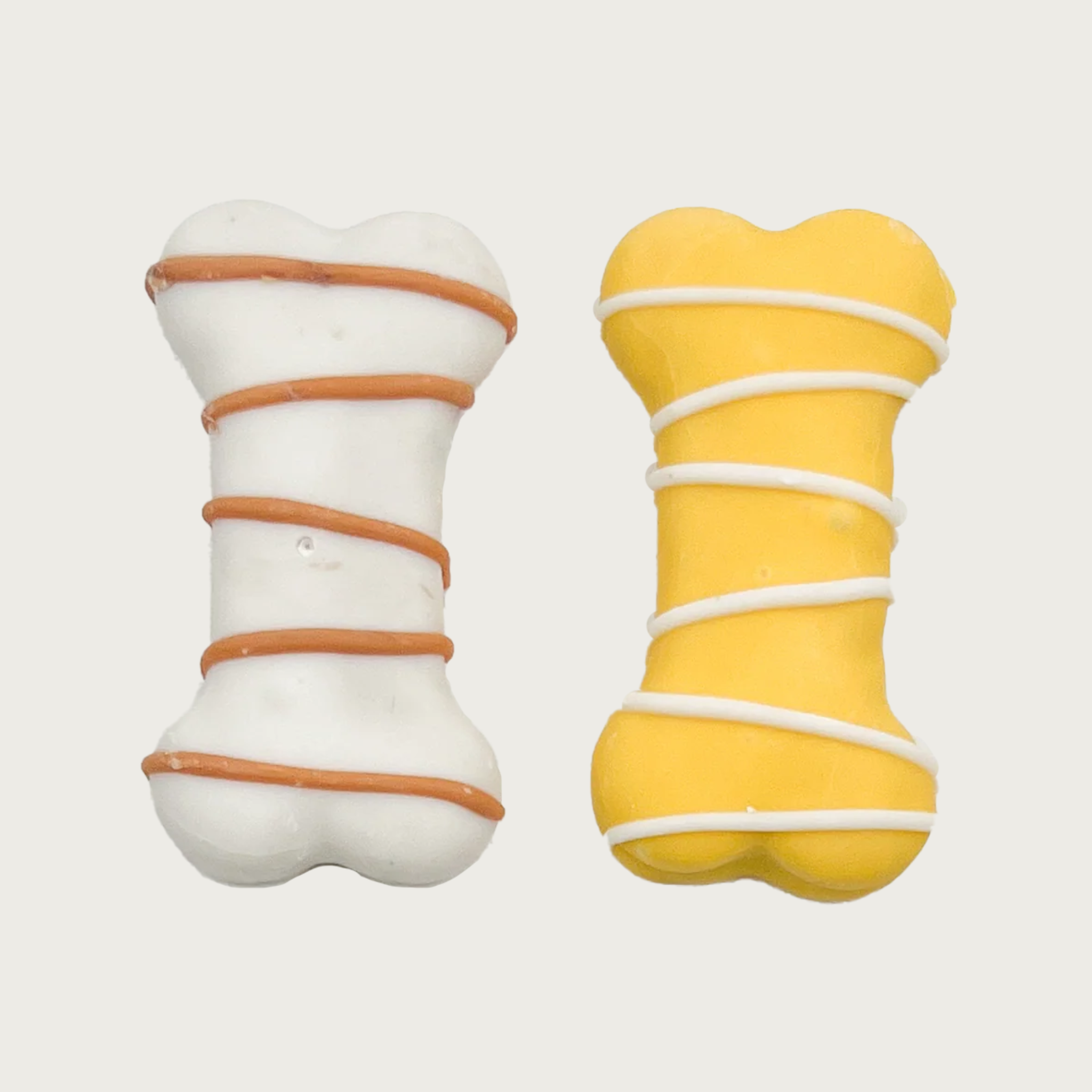 Two bone-shaped dog cookies, side by side. On the left is a white bone with a brown drizzle, on the right is a yellow bone with a white drizzle.