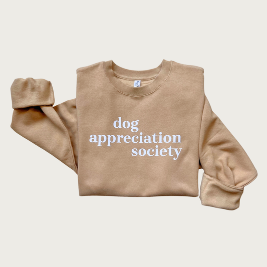 Tan, crewneck sweatshirt with 'dog appreciation society' in white lower case text, in the center of the shirt. 