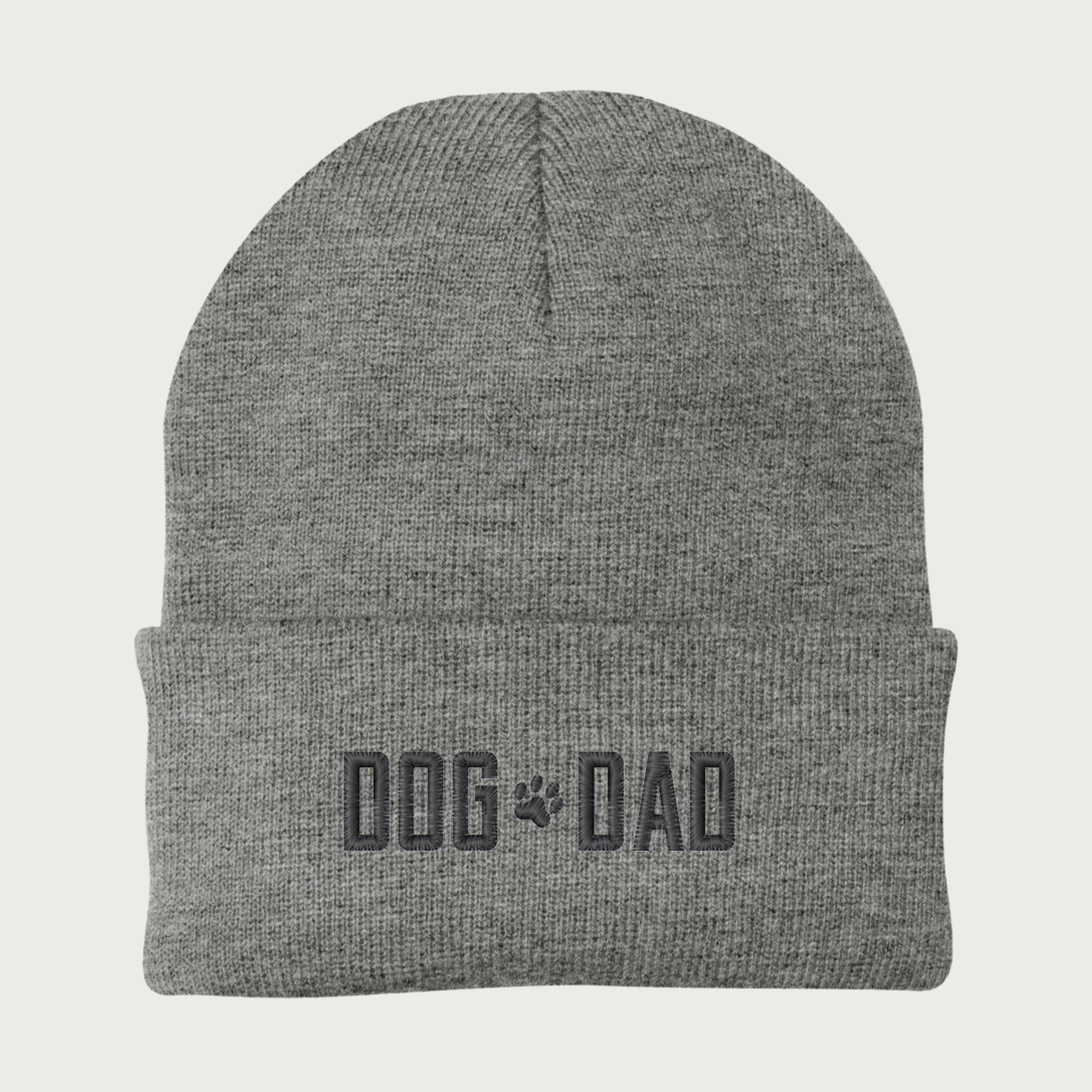 Heather gray beanie (winter cap) with 'DOG DAD' in all caps embroidered on the cuff, with a small paw print between the words. Embroidery is dark gray.