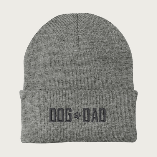 Heather gray beanie (winter cap) with 'DOG DAD' in all caps embroidered on the cuff, with a small paw print between the words. Embroidery is dark gray.