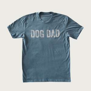 Medium shade of Indigo blue crew neck t-shirt with "Dog Dad" on chest in large, all caps, distressed white text.