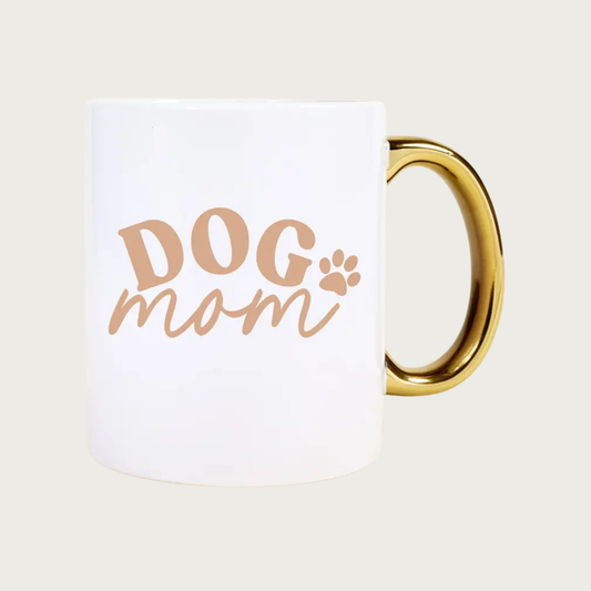 White mug with 'DOG mom' text and paw print in tan with shiny gold handle. "DOG" is in all caps and "mom" is in lower case script text.