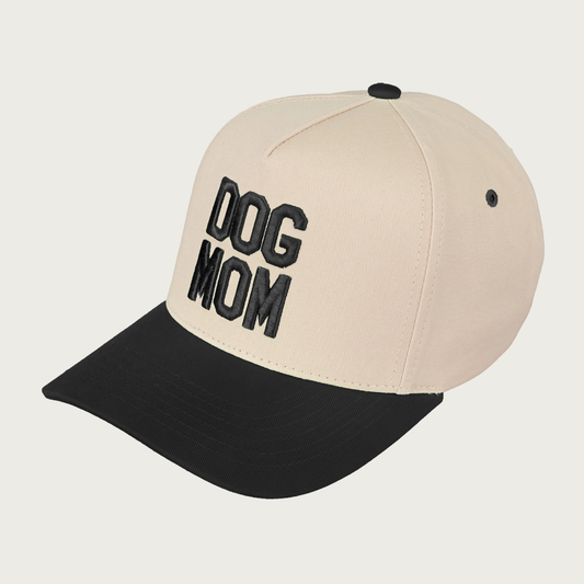 Trucker cap with black embroidered 'DOG MOM' text on front. Bill and accents are black, hat body is light beige.