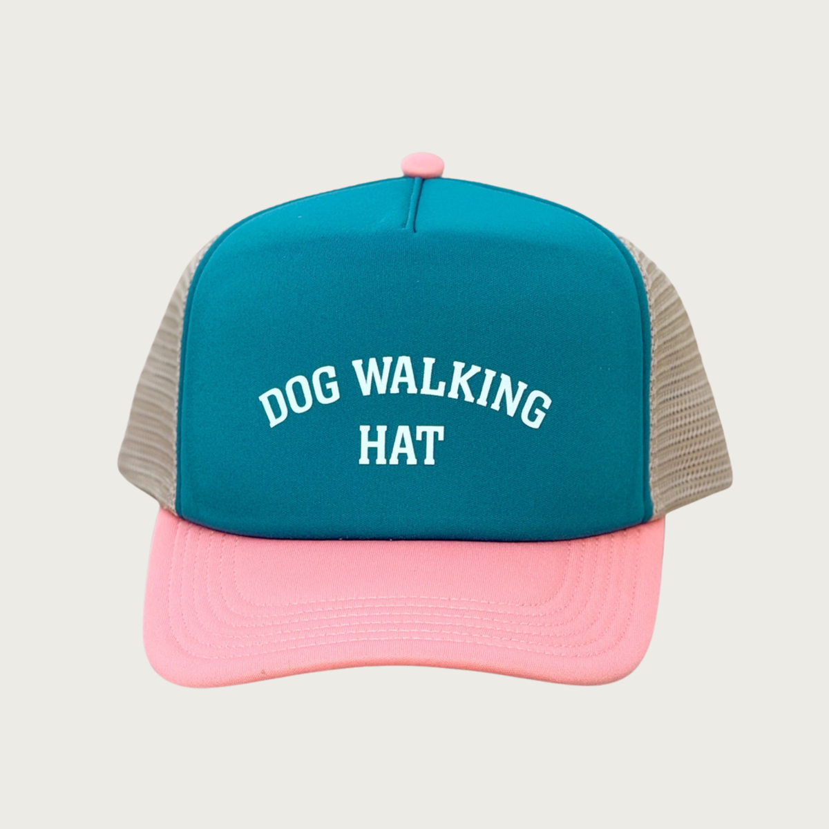 A trucker-style cap with a teal front panel, coral brim, and beige mesh side panels. The front panel features the text 'DOG WALKING HAT' in white arched all caps letters.
