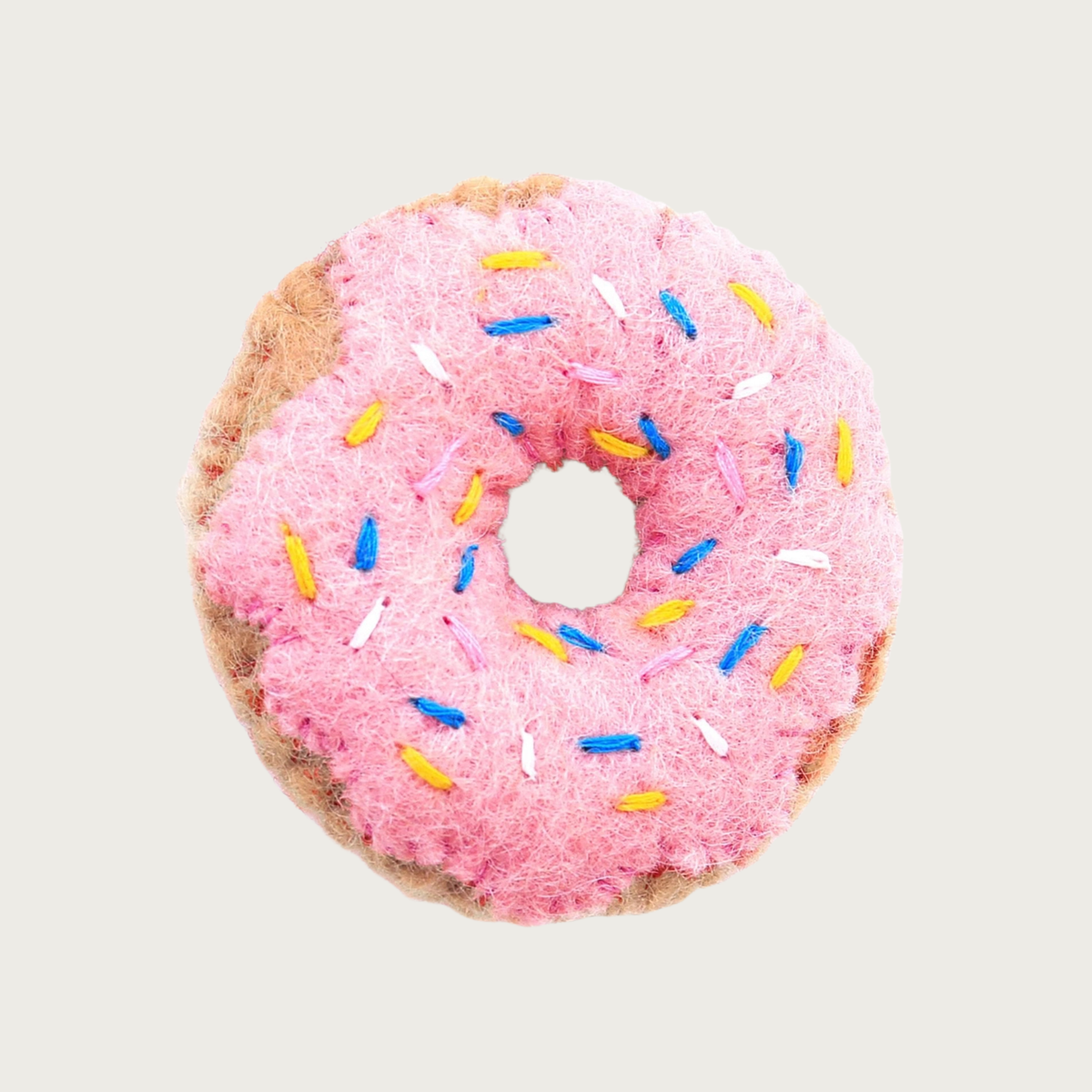 A felted wool donut cat toy with pink frosting and blue, yellow & white sprinkles.