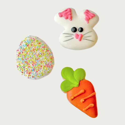 Hand-decorated Easter themed mini dog cookies designed to look like a white bunny face, a carrot, and an Easter egg with multi-colored non-pareils.