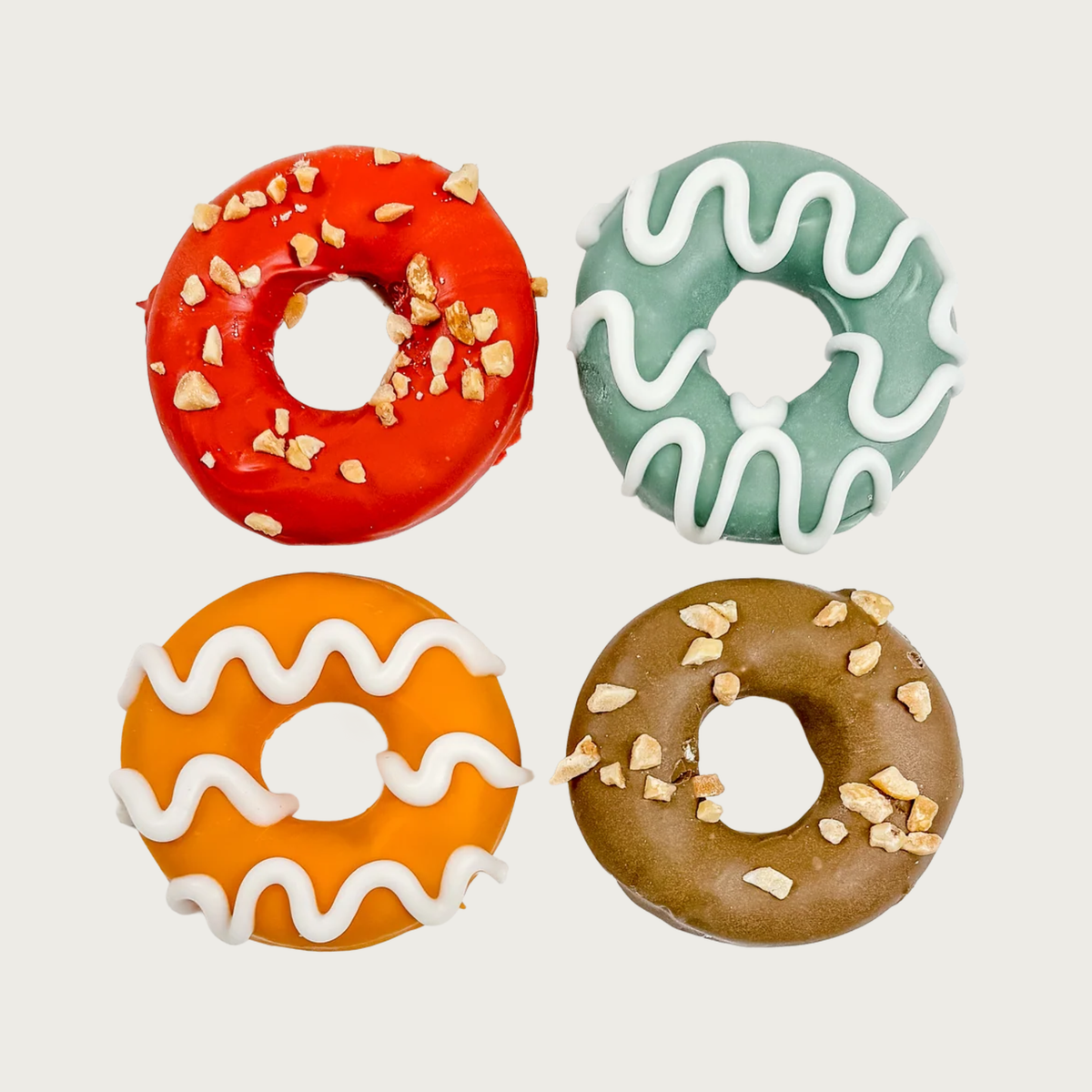 Four mini donut shaped dog treats, laid out in a grid. They all have solid colors as a base; either red, light teal, orange, or brown. They are decorated with either crushed peanuts or white squiggle icing.