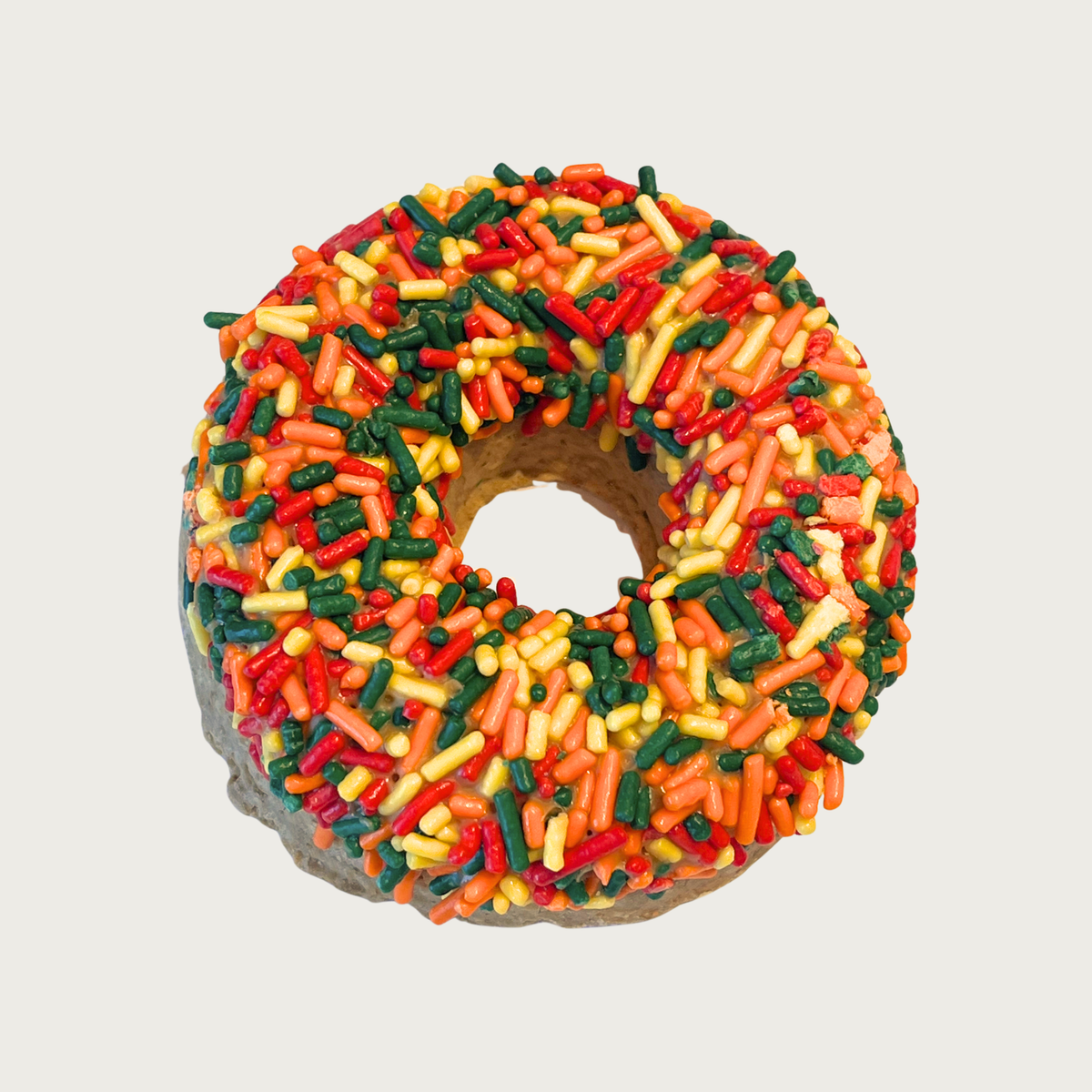 Thick, donut shaped dog cookie decorated with bright, multi-colored autumnal colored sprinkles.