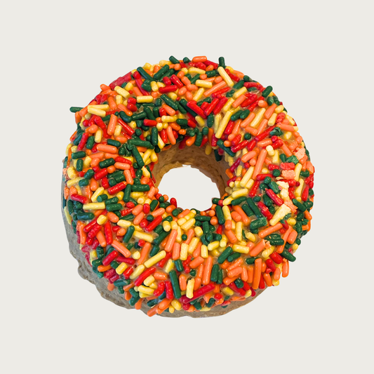 Thick, donut shaped dog cookie decorated with bright, multi-colored autumnal colored sprinkles.