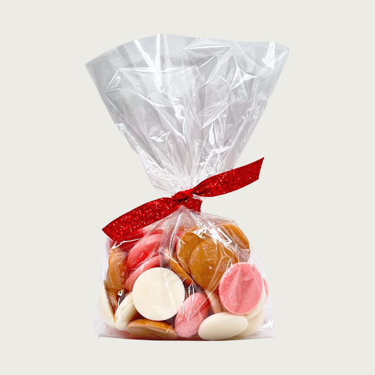 Clear cellophane bag tied with red ribbon of Wet Nose Guilty Pleasures NeaPAWlitan Flavor Dog Treats. Tan, cream, and pink disc-shaped treats are inside. 4 oz.