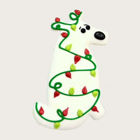 Decorative dog-shaped cookie for dogs. It's white and draped with a string of red & green Christmas lights. 