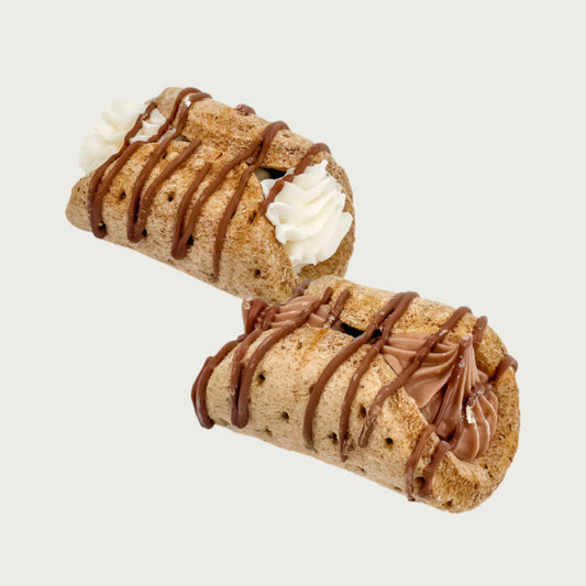Two cannoli shaped dog cookies. The cookie is folded like a taco, with either white or light brown filling. They are drizzled with brown icing.