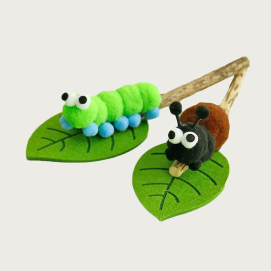 Toy features a plush insect mounted on a felt leaf and silver vine stick. Two styles pictured: green and blue caterpillar or brown and black ant with antenna.