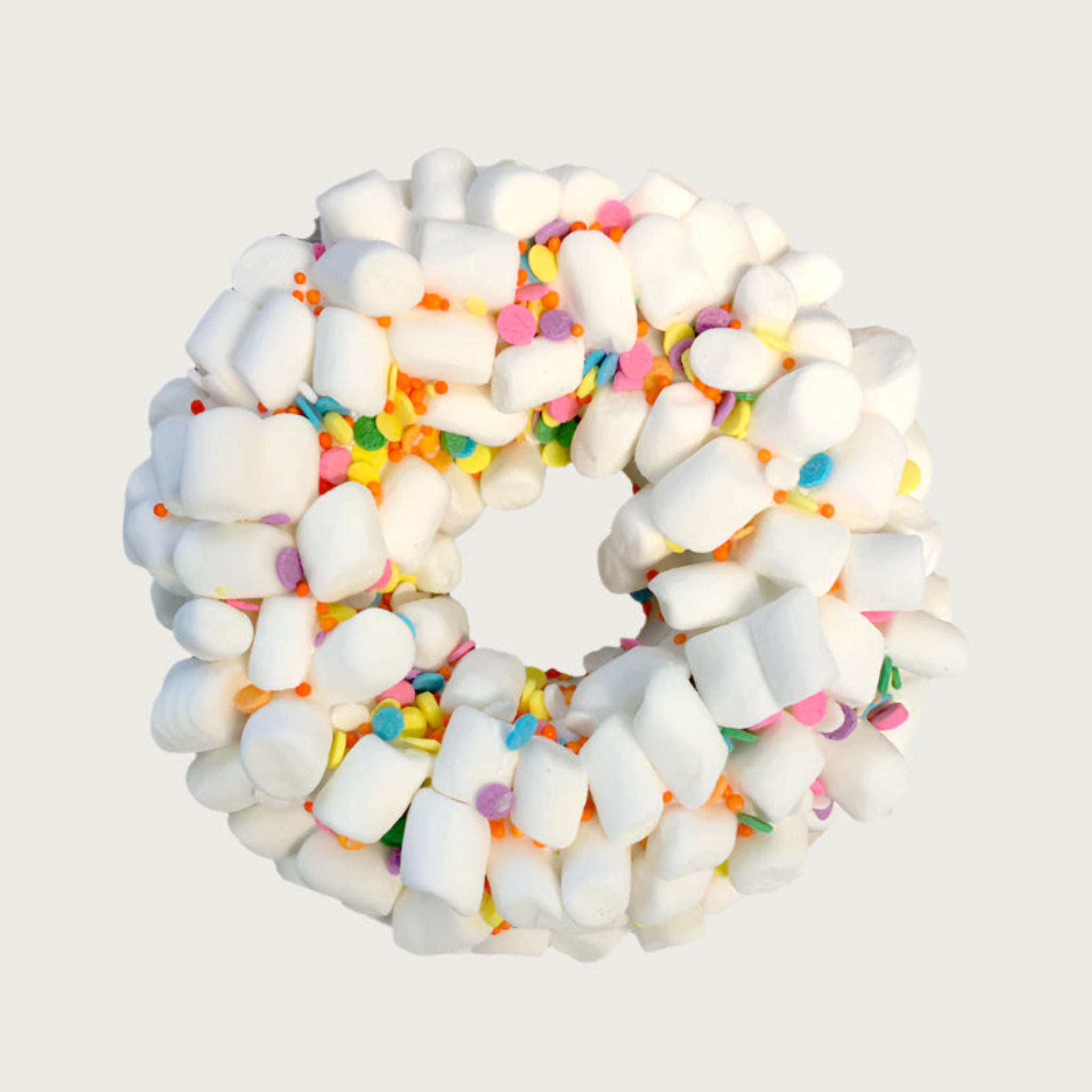 Thick, donut-shaped dog cookie covered with mini marshmallows and decorated with multicolored sprinkles.
