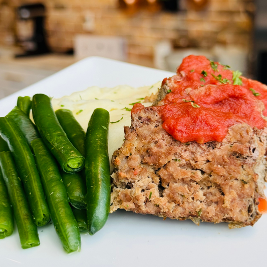 Sliced meatloaf with tomato sauce, green beans, and mashed potatoes on a plate.