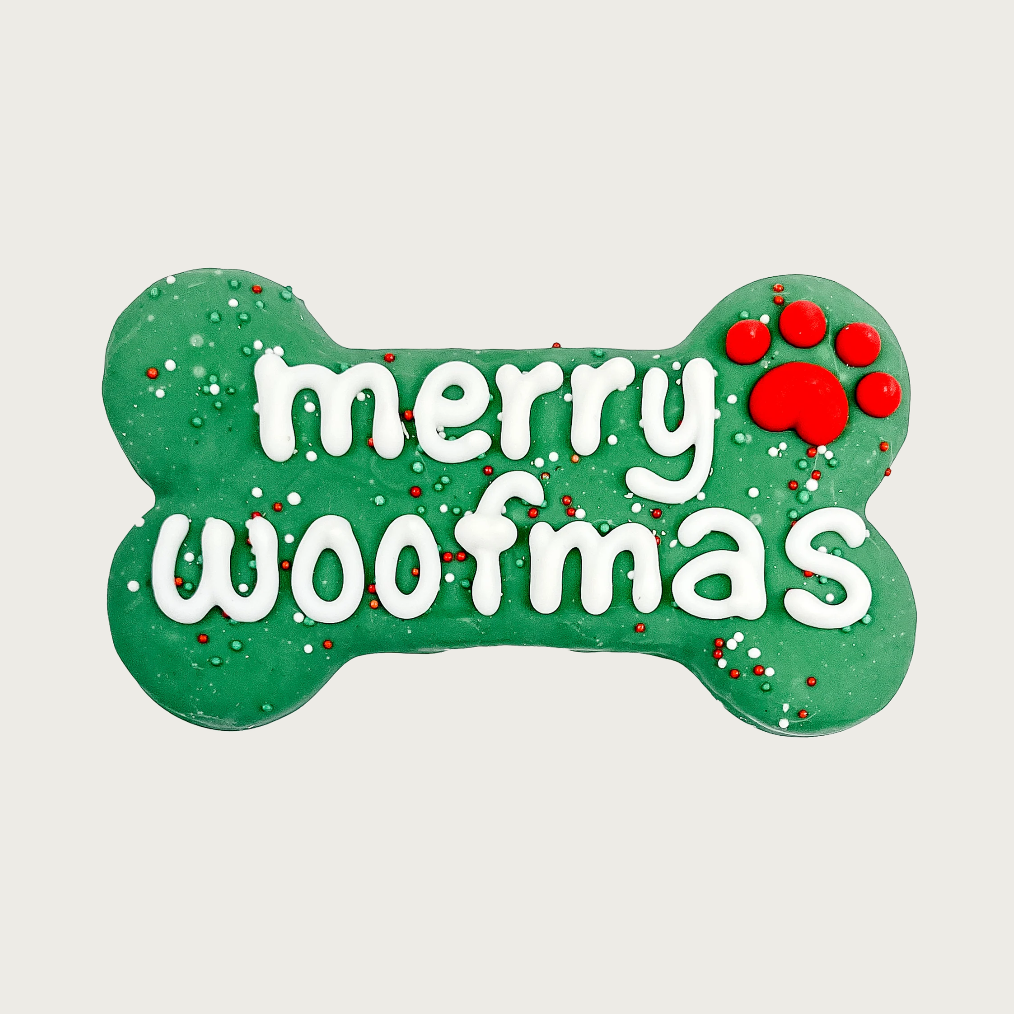 Large bone-shaped dog cookie, covered in green coating. Decorated with white text that reads "Merry Woofmas", accented with a red paw print and red, white & green nonpareils.