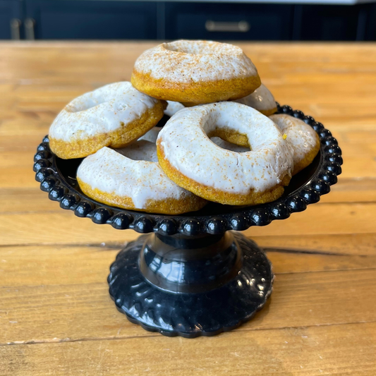Mini pumpkin donuts with white glaze stacked on a black decorative stand.