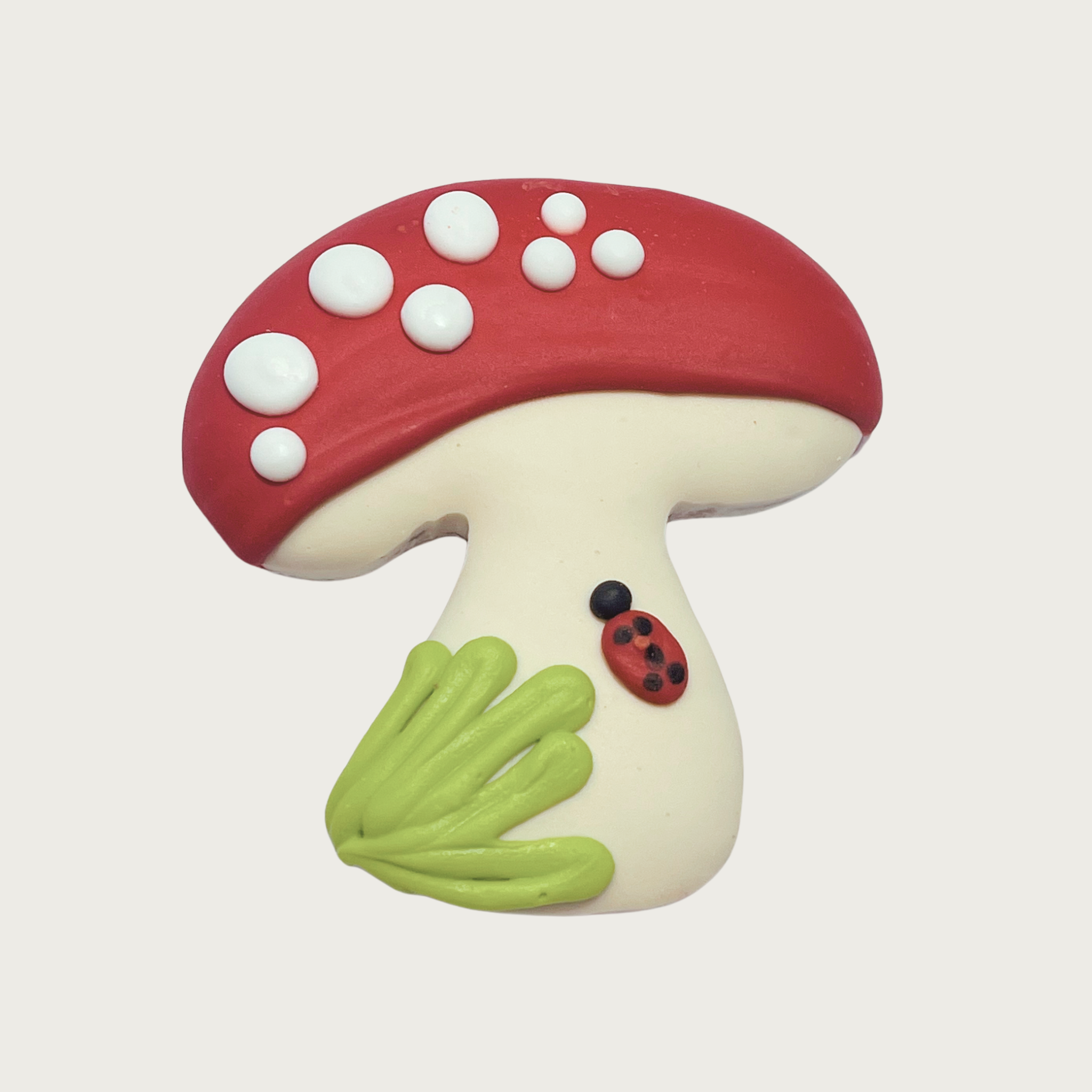 Decorated dog cookie shaped like a mushroom. It has a red cap with white spots, white stem, and is accented with a patch of light green grass and a black & red ladybug.