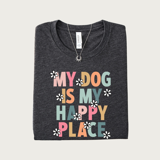 A folded dark heather gray t-shirt with a colorful graphic that reads 'MY DOG IS MY HAPPY PLACE' in shades of pink, orange, and blue-green all caps letters, accented with small black & white daisy flowers.