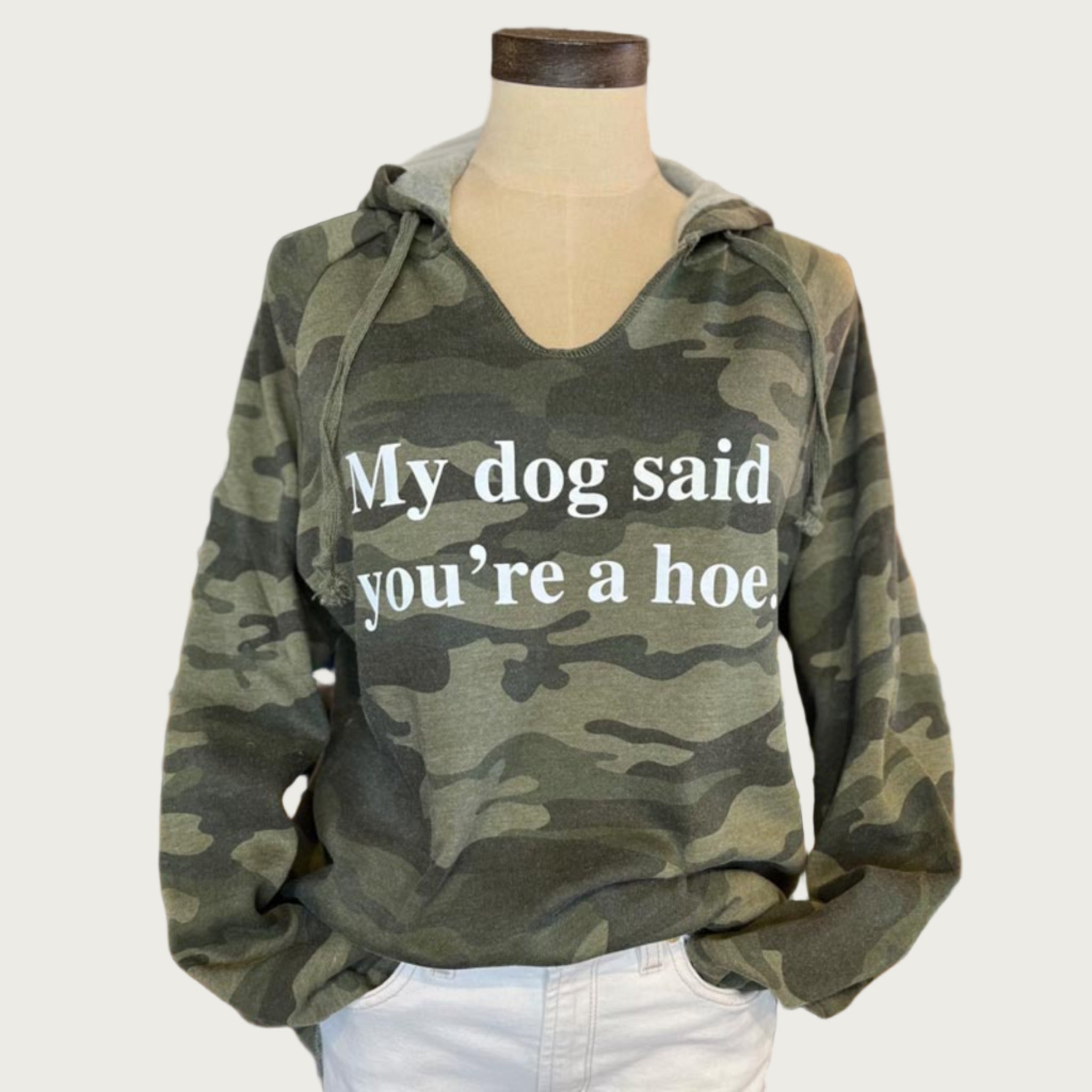 A camouflage hoodie in shades of olive green, with a slight v-neck. White text on chest reads "My dog said you're a hoe."
